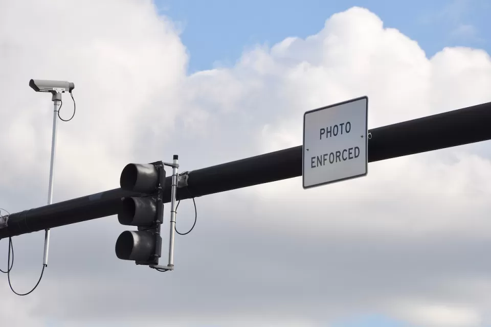 Traffic light on overhead pole with traffic camera and "Photo Enforced" sign